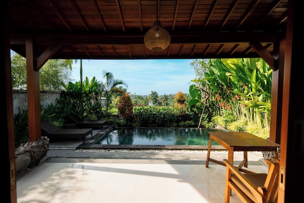 Un espacio al aire libre cubierto con piscina, mobiliario de madera y exuberante vegetación tropical.