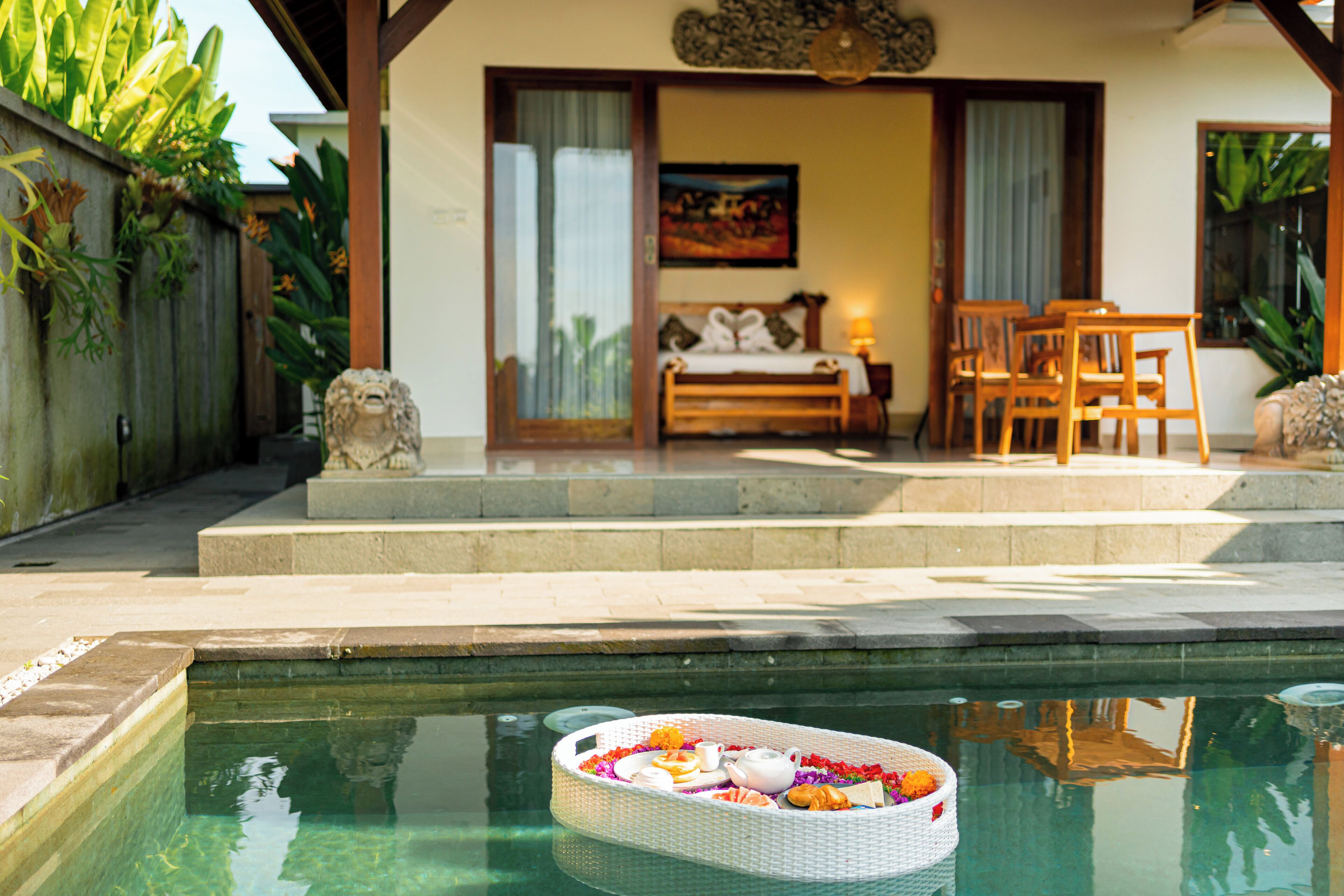 A pool with a floating tray of food and a wooden deck with a sofa and chairs.
