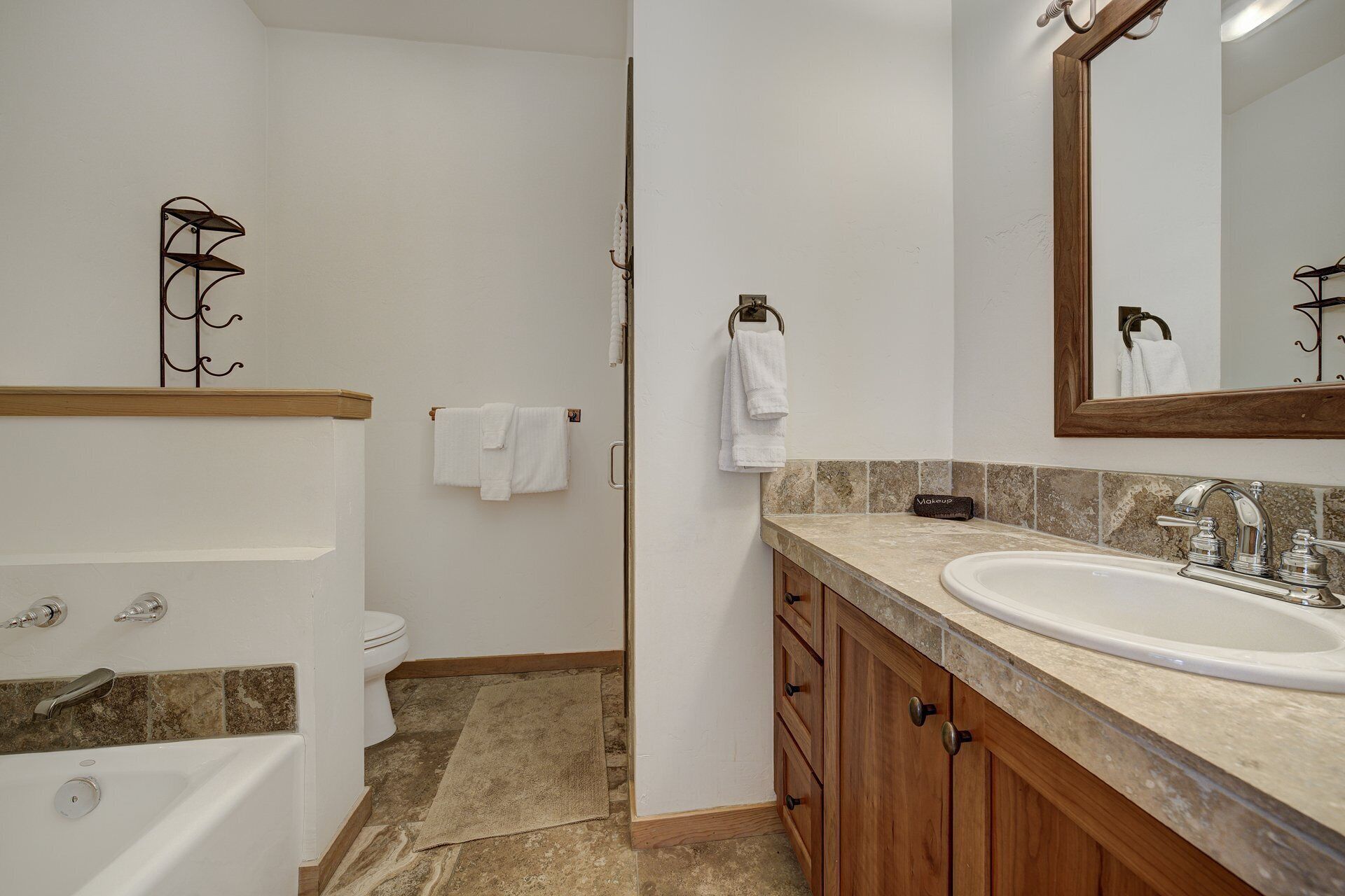 A modern bathroom with a bathtub, a sink, and a toilet. There are towels hanging on hooks and a mirror above the sink.