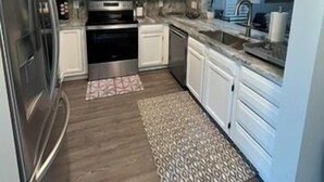Une cuisine avec des meubles blancs, des appareils en acier inoxydable, un tapis à motifs et un mur bleu.