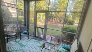 Une véranda avec un toit en verre, un tapis à motifs verts, un canapé avec des coussins et une petite table.