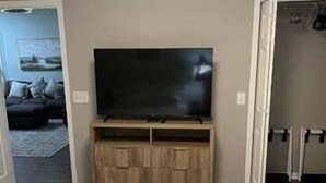 Une chambre d’hôtel dotée d’un grand téléviseur à écran plat fixé sur un meuble en bois, de deux lits simples et d’une porte donnant sur une autre pièce.
