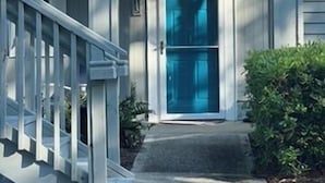 Une maison à deux étages avec un porche à l’avant, une porte bleue et un escalier menant à l’entrée.