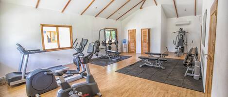 A spacious gym with various exercise equipment, wooden floors, and large windows.