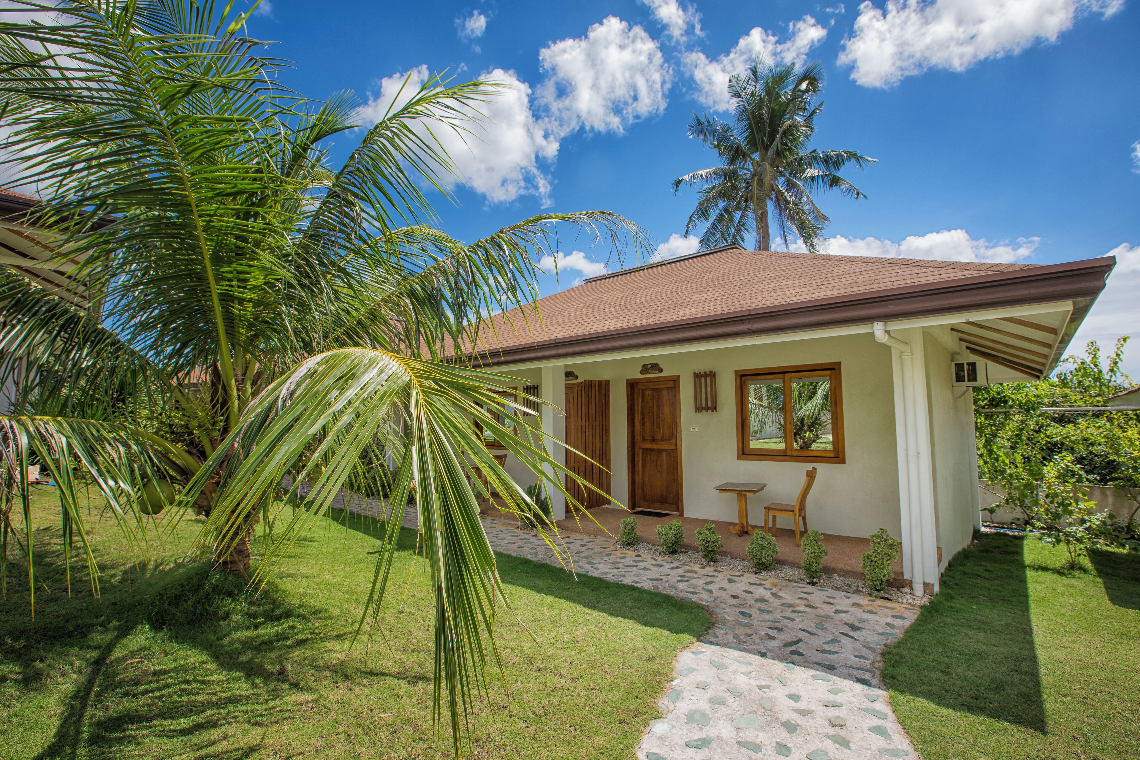 A house with a tiled roof, a small porch, and a palm tree in the yard.