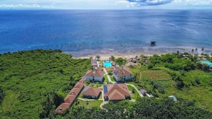 Vue aérienne d’une station balnéaire comprenant plusieurs bâtiments de style bungalow, une piscine centrale et une plage.