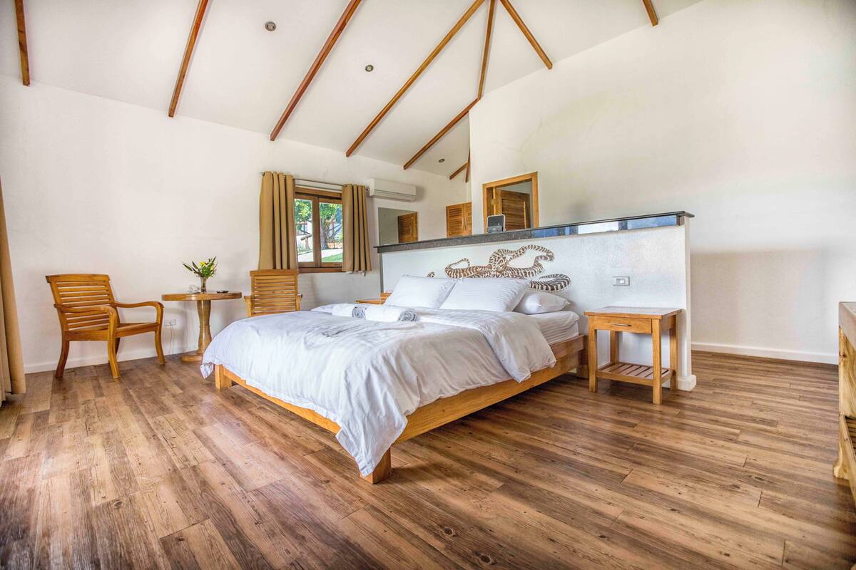 Une chambre à coucher avec un lit en bois, une petite table, une chaise et un miroir au mur.