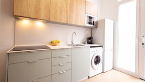Cocina compacta con armarios de madera, microondas, pileta, cafetera y lavadora.