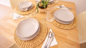 Una mesa de comedor dispuesta con platos, vasos y cubiertos, rodeada de individuales tejidos.
