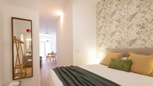 Un dormitorio con una cama grande, un espejo, un tendedero de madera y un baño al fondo.