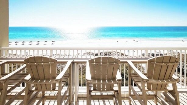 Ein Balkon mit drei Holzstühlen und Blick auf einen Strand.