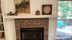 A living room with a brick fireplace, a round table with a book, a clock, and a painting on the wall. - Pollys Place for bird lovers - Private, Close to Gallatin-Sleeps 10-Pet Friendly (Portland)