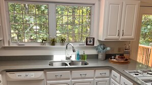 A kitchen with white cabinets, a stainless steel sink, and a window with a view of trees. - Pollys Place for bird lovers - Private, Close to Gallatin-Sleeps 10-Pet Friendly (Portland)