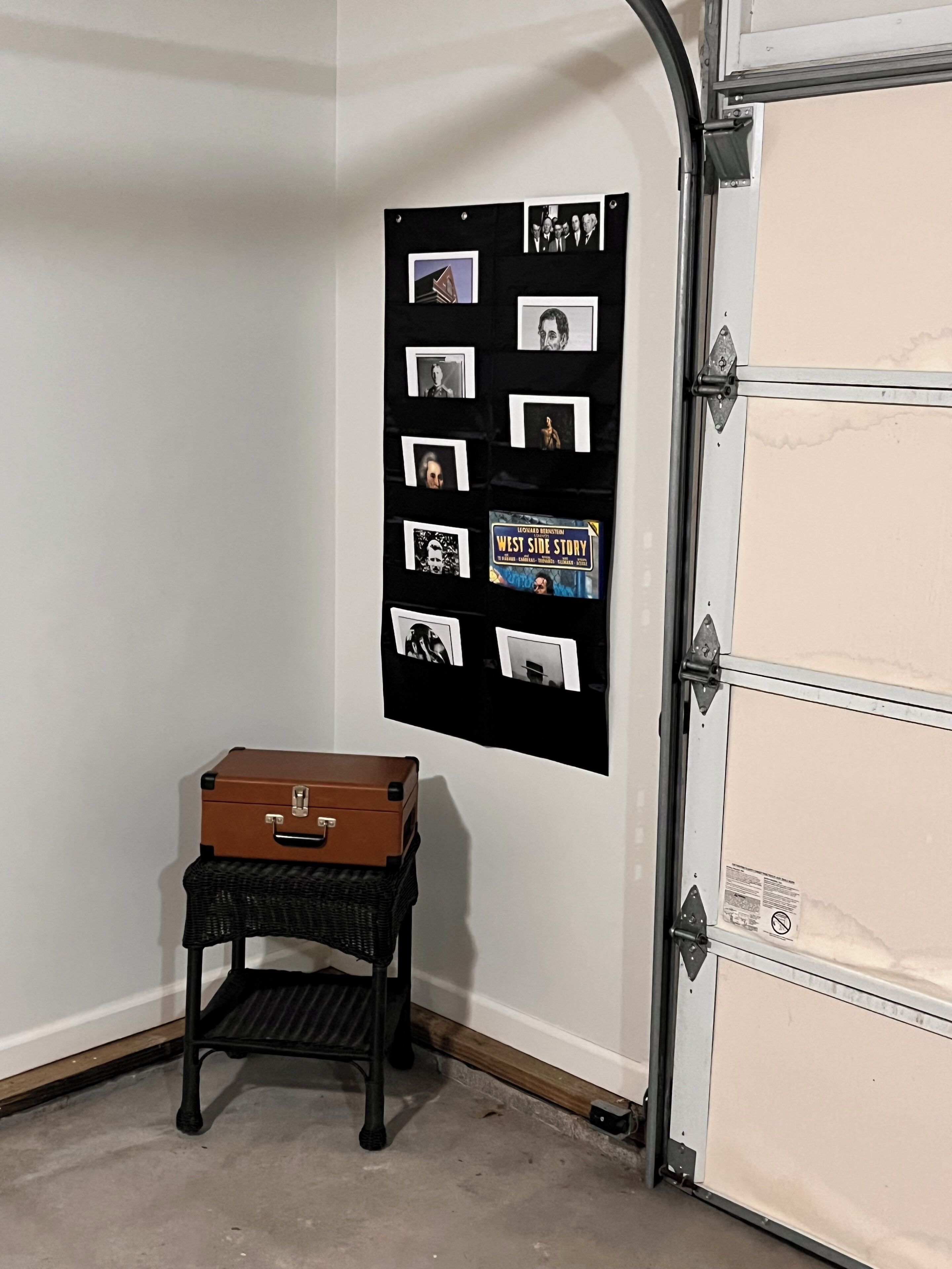 Et værelse med et billedmontage på væggen, en kuffert på et lille bord og en garageport.