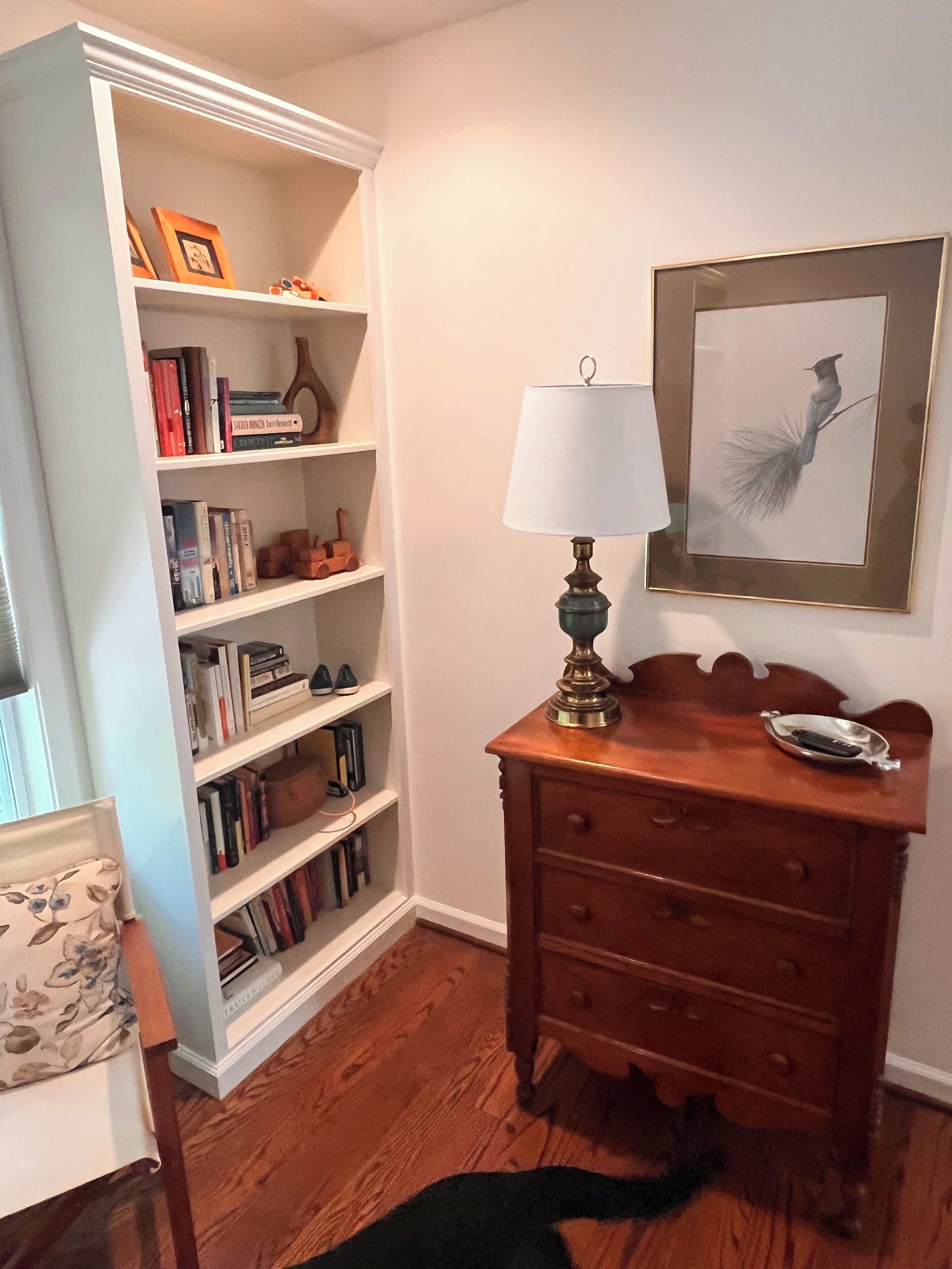 Ein Zimmer mit einem Holzkasten, einer Lampe, einem Bücherregal und einem gerahmten Bild an der Wand.