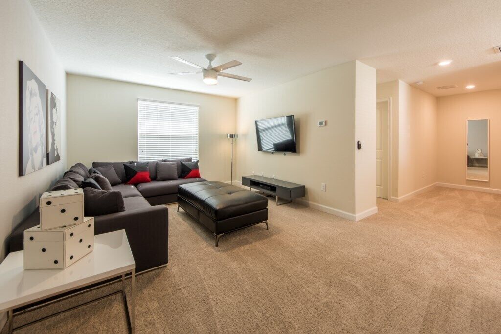 A living room with a sofa, ottoman, and a flat-screen TV.