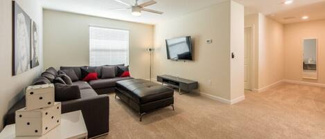 A living room with a sofa, ottoman, and a flat-screen TV.