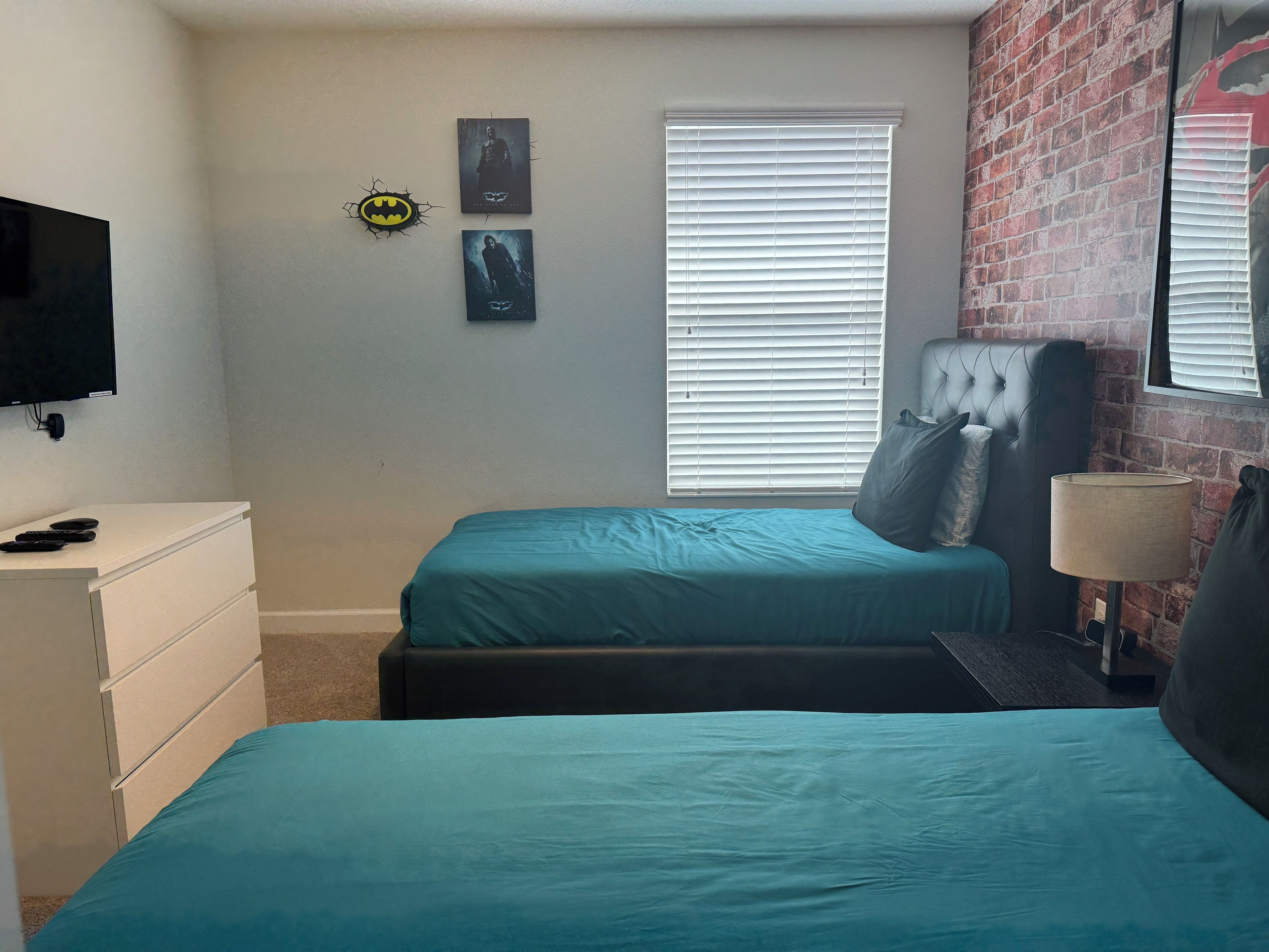 A bedroom with two beds, a TV, a dresser, and a brick wall.