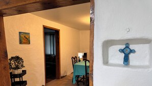 Un pasillo con piso de madera, un comedor con mesa y sillas, una planta en maceta y una cruz colgada en la pared.