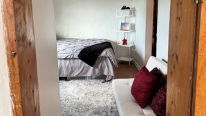 Un dormitorio con cama, sofá blanco, alfombra mullida y ventilador de techo.