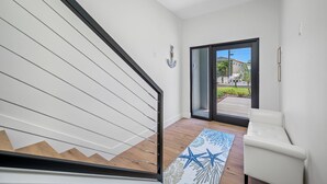 Ein modernes Interieur mit einer Treppe, einem weißen Sofa und Blick durch eine Glastür nach draußen.