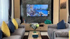 Een moderne woonkamer met een flatscreen televisie bevestigd aan een donkere marmeren muur, twee grijze banken met gele en blauwe kussens, een houten salontafel en een kleine bijzettafel met een bloevas.