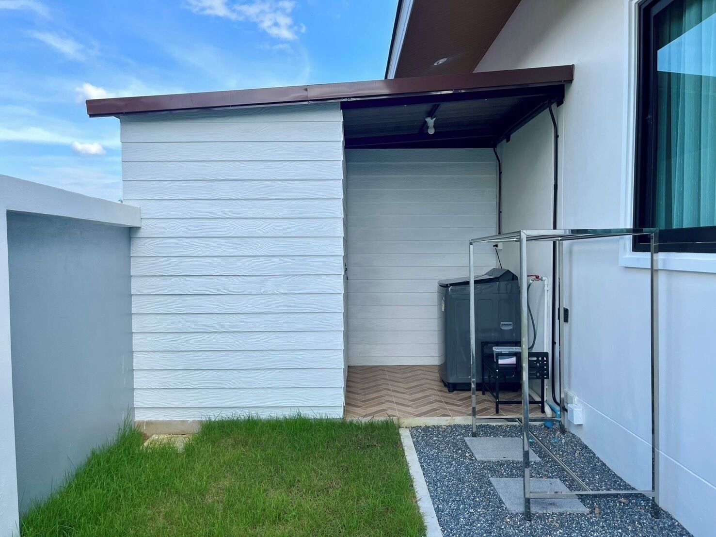 A modern building with a white exterior, a covered outdoor area with a heater, and a small grassy patch.