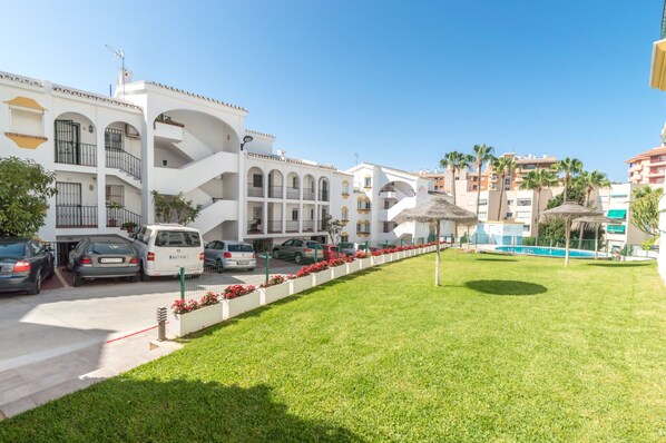 A hotel with a white facade, multiple balconies, a swimming pool, and a well-maintained lawn.