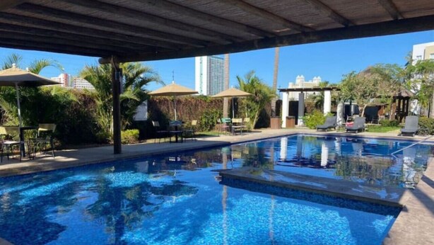 Une piscine dotée d’un espace couvert, entourée de palmiers et de chaises longues.