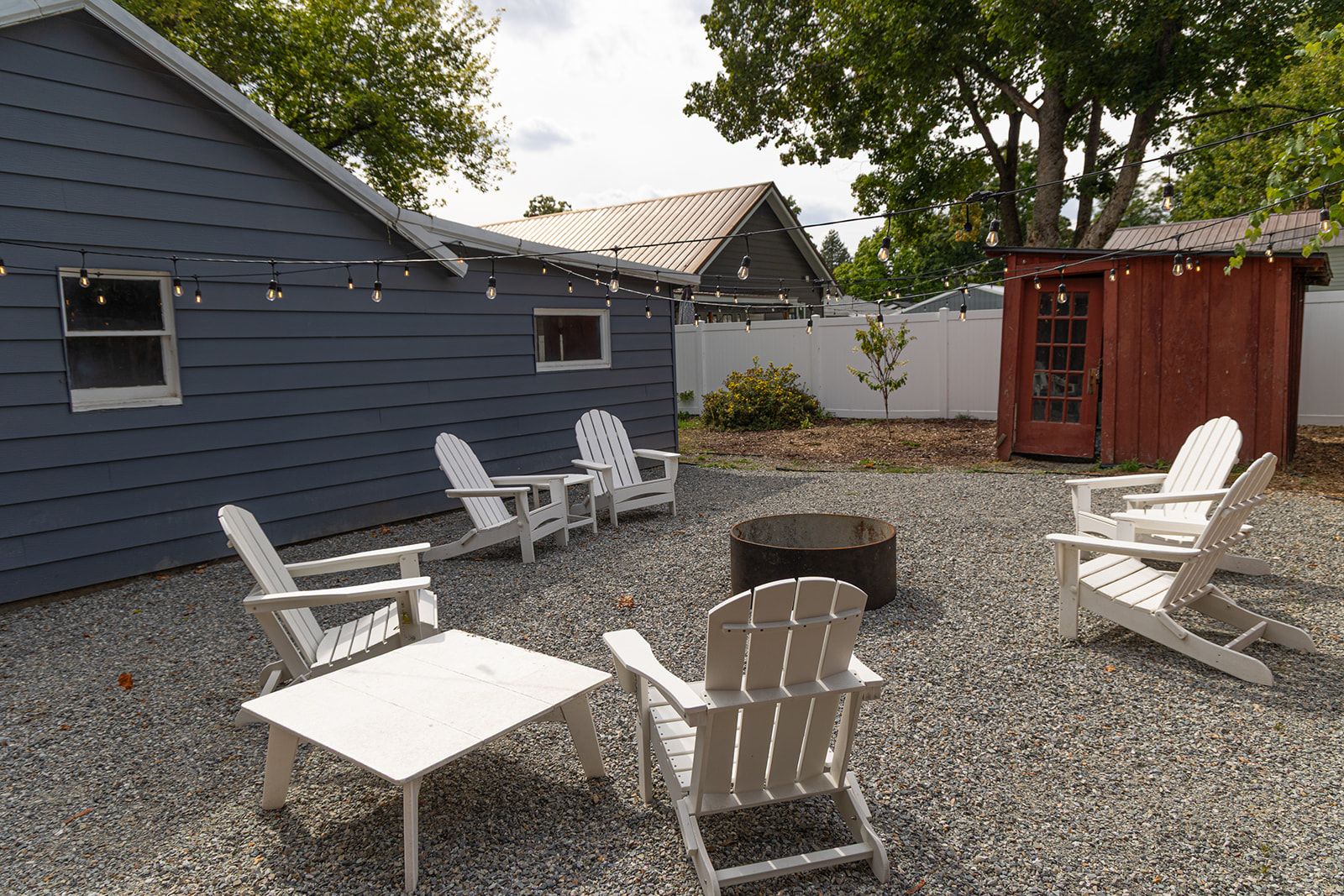 Een terras met Adirondack-stoelen, een vuurkorf en sfeerverlichting.