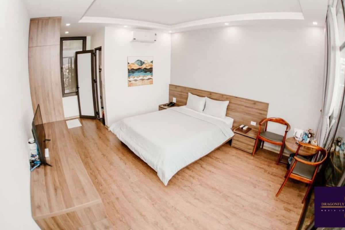 Un dormitorio moderno con piso de madera, una cama con ropa de cama blanca, una mesita de noche, una silla y un cuadro en la pared.