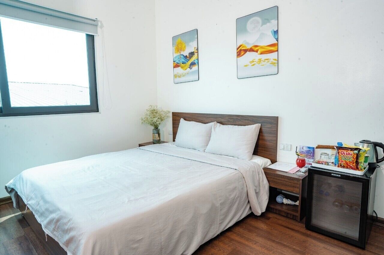 A hotel room with a bed, a small desk with a refrigerator, and two paintings on the wall.