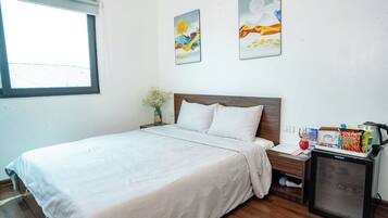 A hotel room with a bed, a small desk with a refrigerator, and two paintings on the wall.