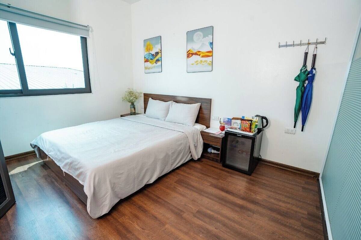 Una cama bien hecha en una habitación con suelo de madera, una mesita de noche pequeña con una lámpara y dos cuadros en la pared.