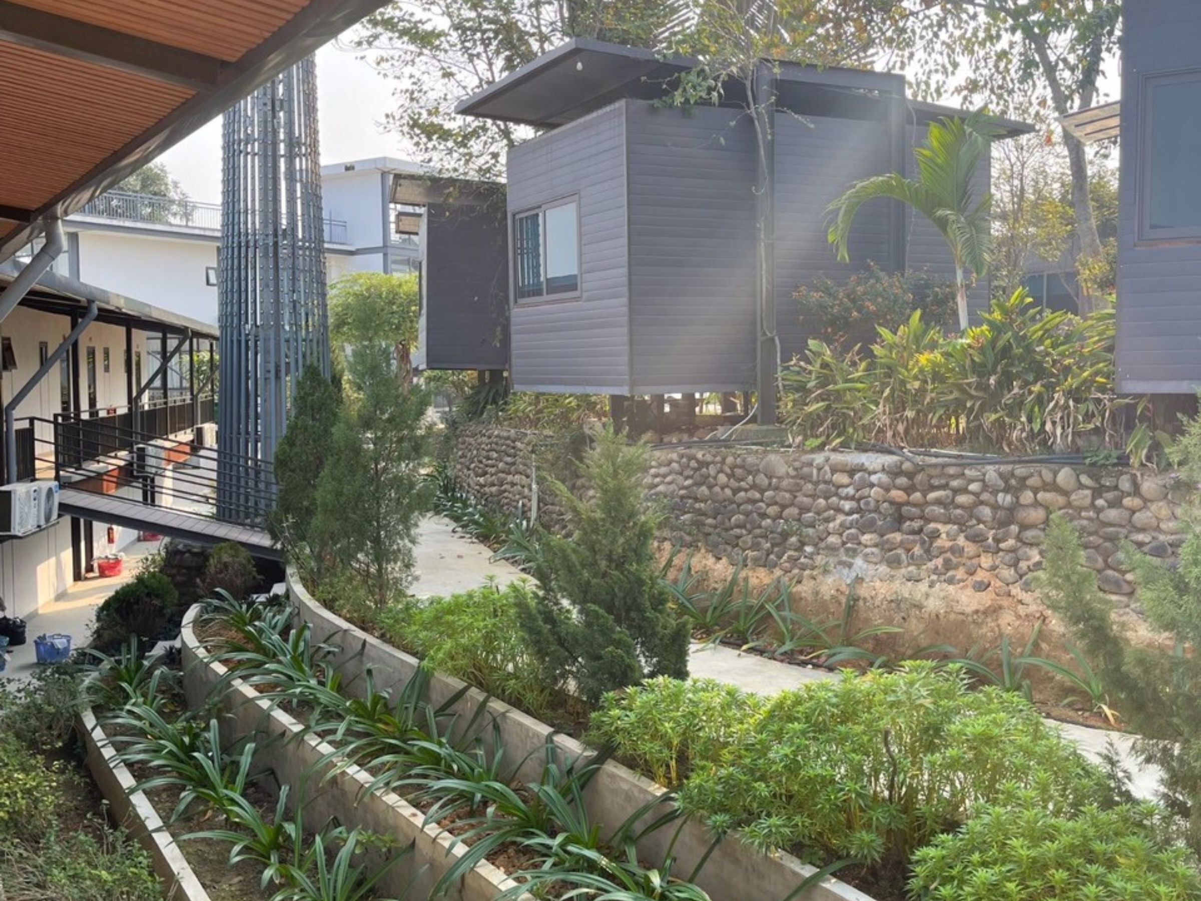 Een moderne woning met een stenen keerwand, een overdekt terras en diverse beplanting.