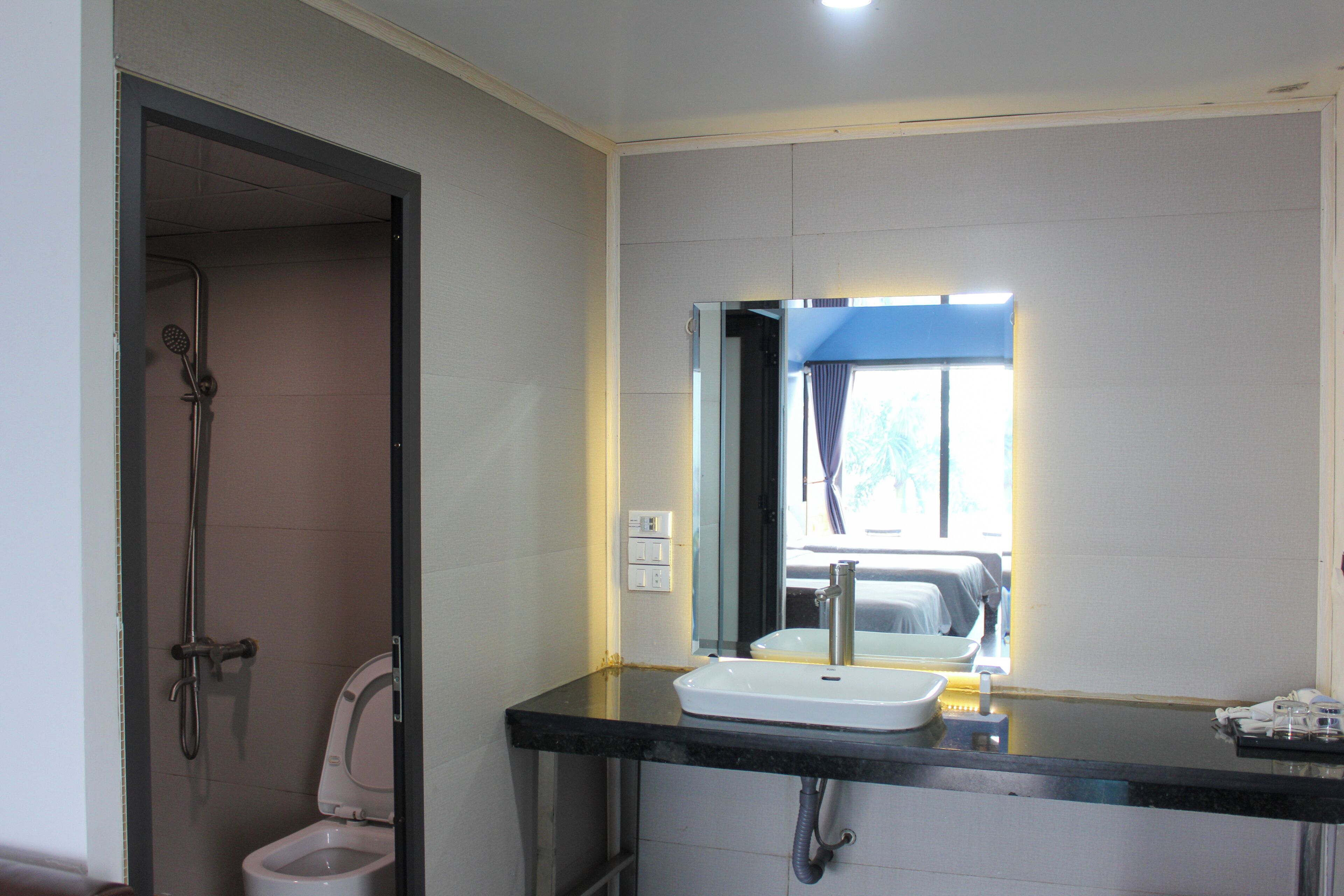 A bathroom with a shower, toilet, sink, and a mirror with a window above it.