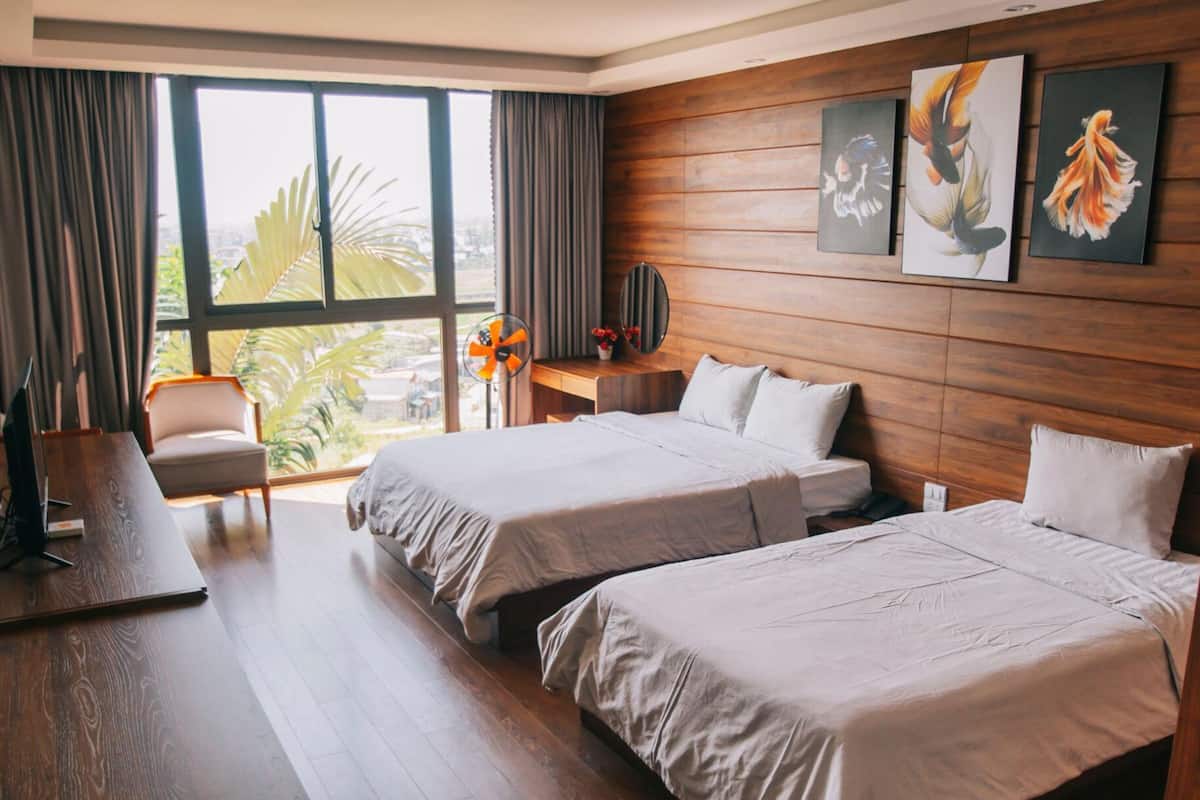 Habitación de hotel con dos camas, un escritorio, una silla y un ventanal con cortinas.