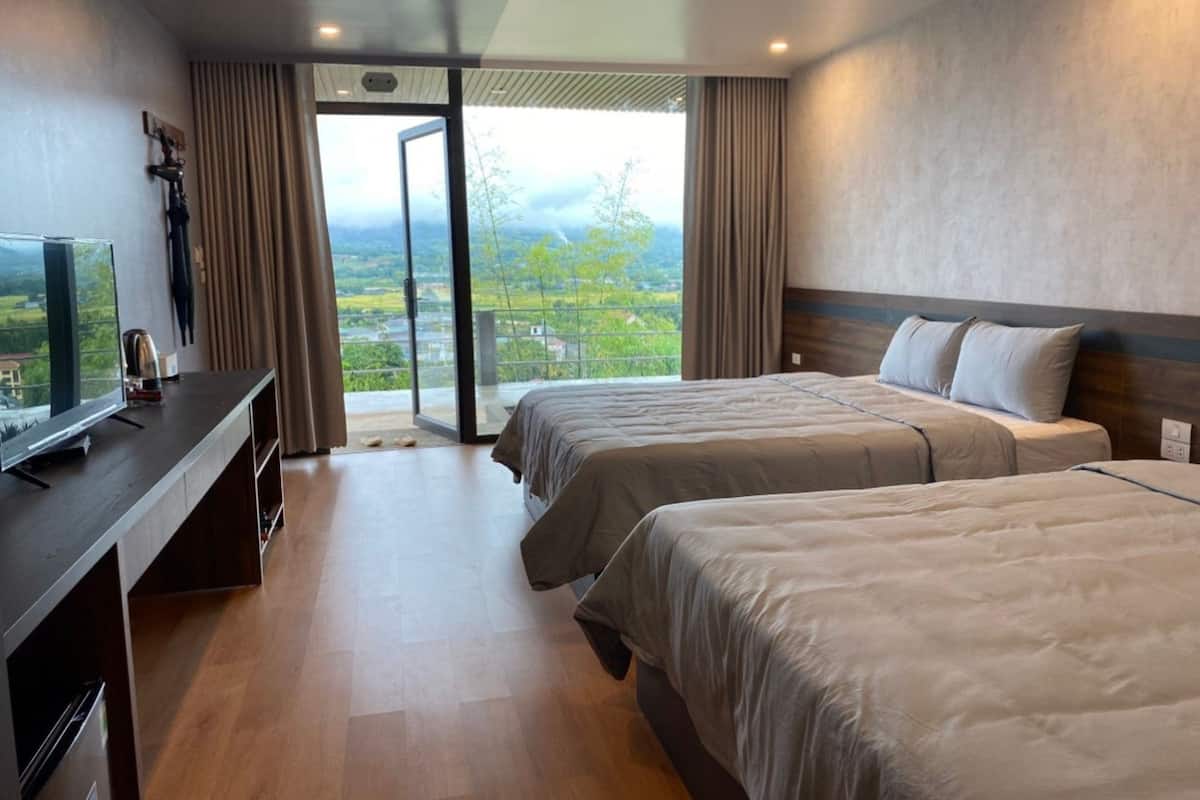 Habitación de hotel con dos camas, televisión y balcón con vistas al campo.