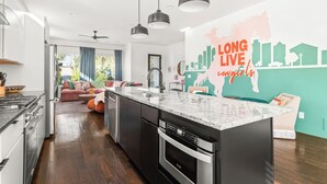 Een moderne keuken met een groot eiland, roestvrijstalen apparatuur, hanglampen en een stadsgezichtsmural op de muur.