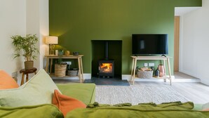 A cozy living room with a green wall, a fireplace, a television, and a sofa with cushions.