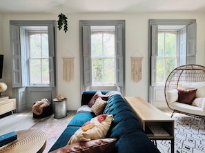 Uma sala de estar aconchegante com um sofá azul, uma mesa de centro de madeira e um painel de parede em macramé.