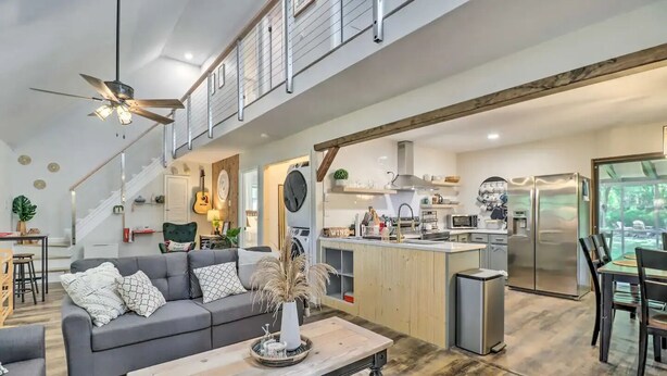 Un espace de vie et de salle à manger moderne, à aire ouverte, comprenant une cuisine, un escalier et une vue sur l’extérieur.
