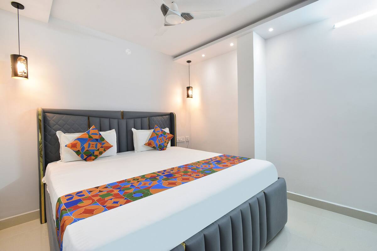 Een moderne slaapkamer met een groot bed, een grijs gestoffeerd hoofdeinde en een kleurrijke bedspread met een geometrisch patroon.