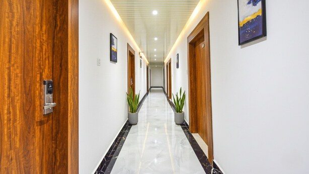 Un pasillo moderno de hotel con puertas de madera, plantas en macetas y cuadros en las paredes.