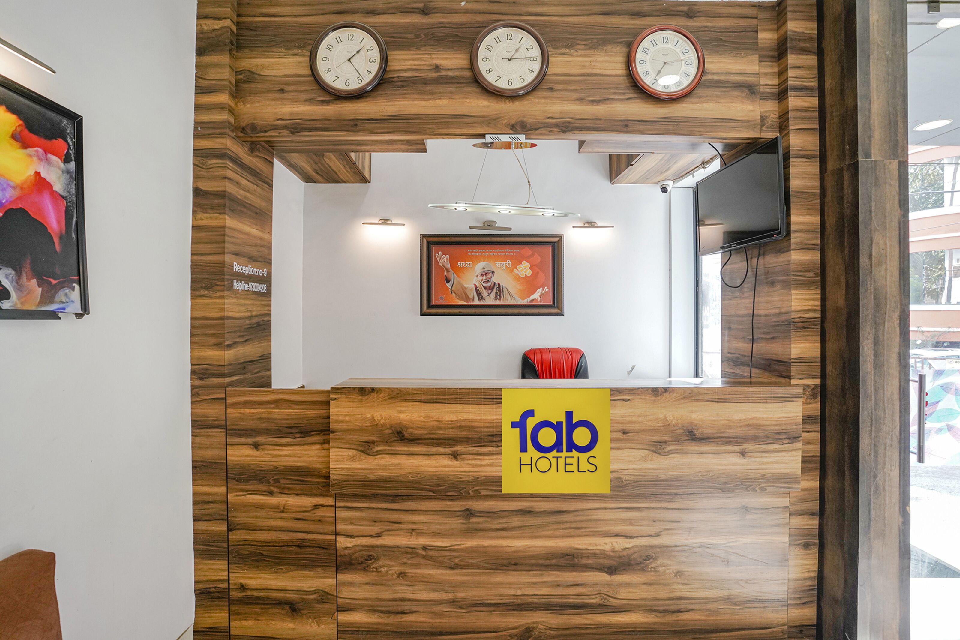 Un comptoir d’accueil avec un revêtement mural en bois, trois horloges, un tableau encadré et un panneau indiquant « fab hotels ».
