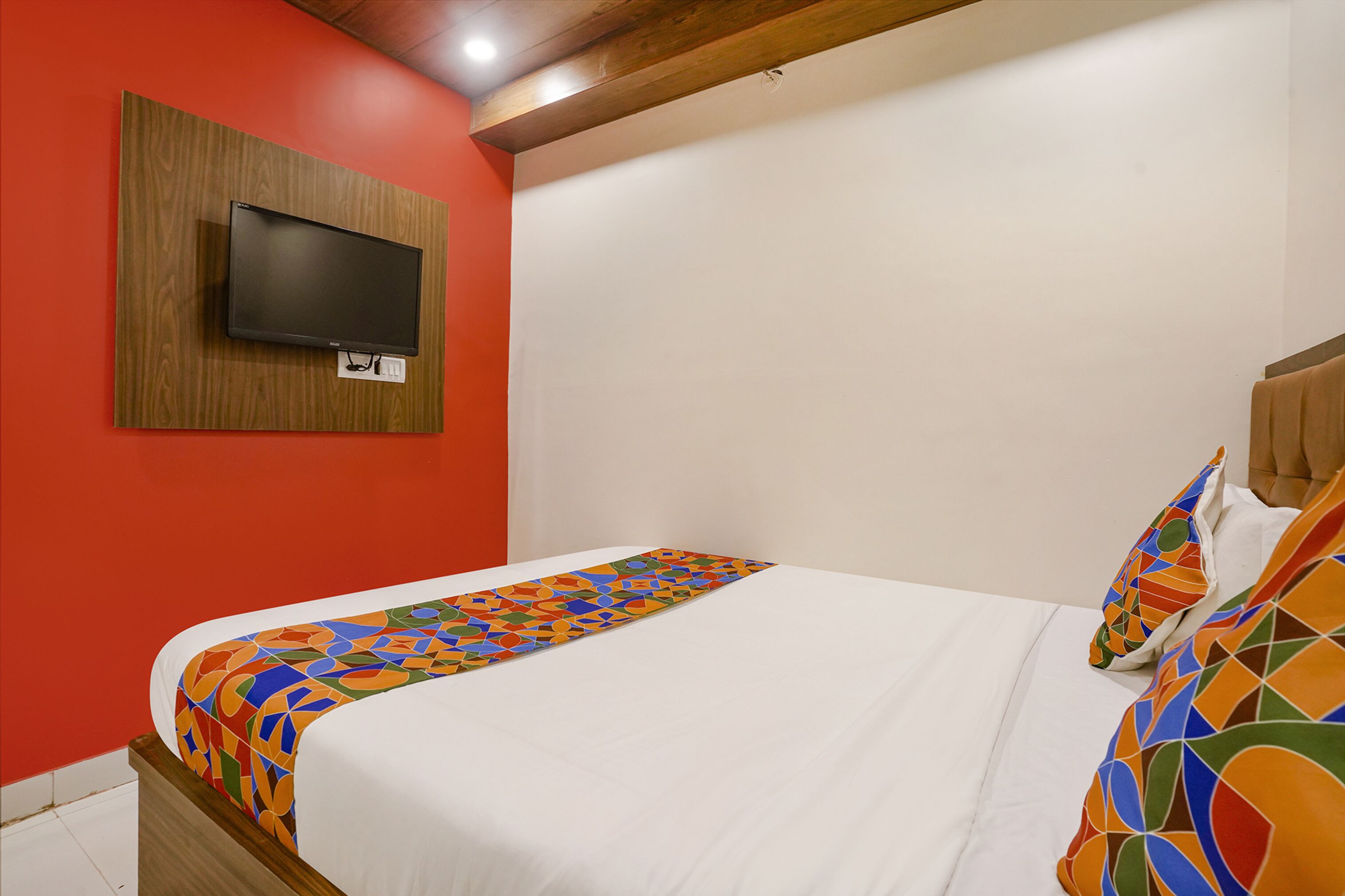 A bedroom with a bed, a TV mounted on a wooden panel, and colorful pillows.