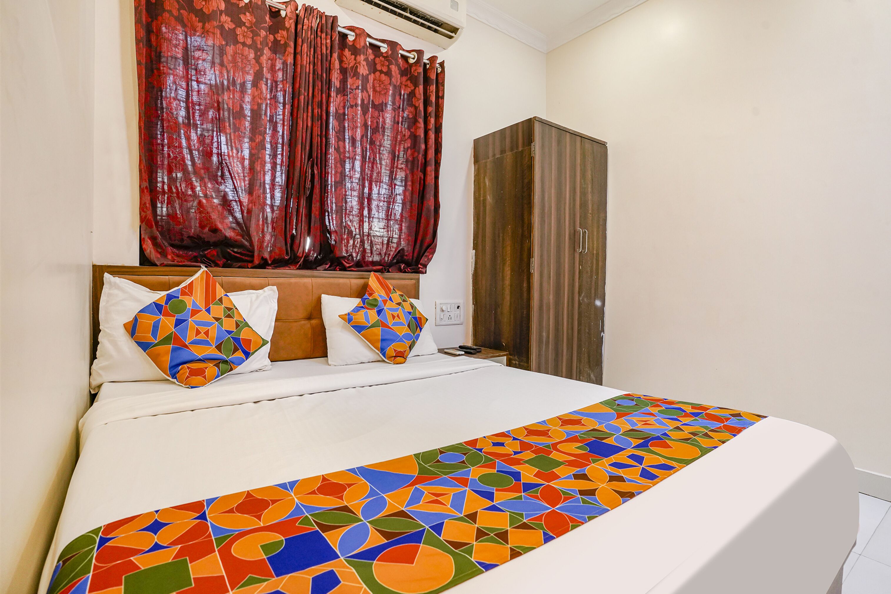 A bed with a colorful geometric-patterned bedspread, a wooden headboard, and two pillows with geometric patterns.