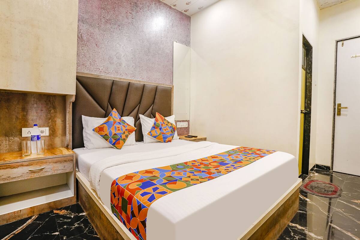 A hotel room with a bed, a nightstand, a mirror, and a door.