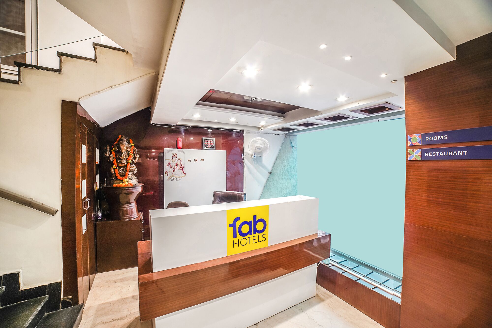 A hotel reception desk with a modern design, a sign indicating the rooms and restaurant, and a statue of a deity.