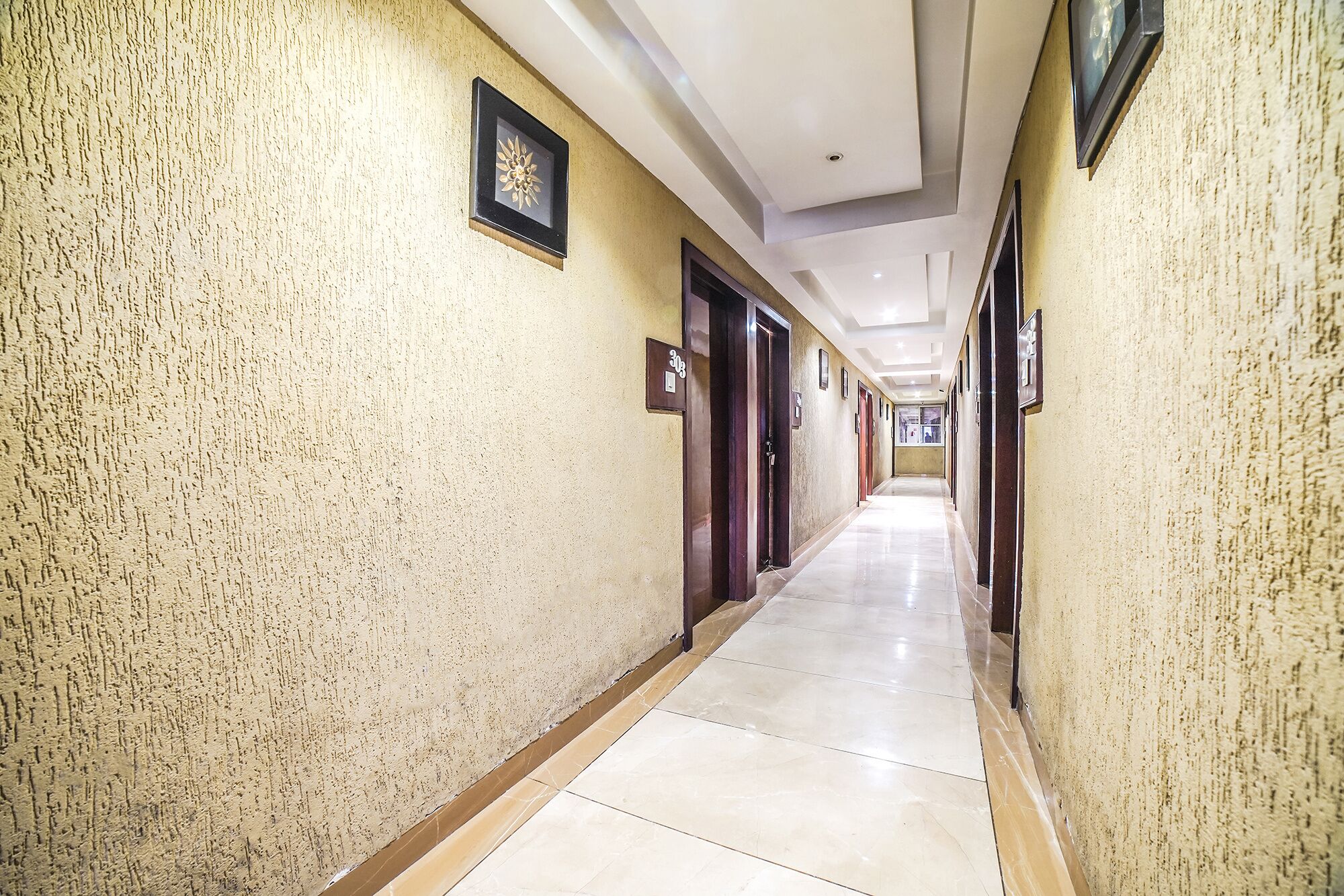 Un largo pasillo bien iluminado con pared texturizada, puertas y suelo de baldosas.